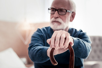 Senior age. Selective focus of elderly mans hands being put on the walking stick while holing it