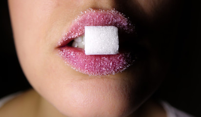 A woman holds a piece of sugar between her pink lips covered with sugar. Concept for eating sweets...