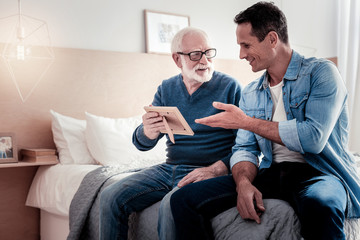 Always in memory. Delighted nice aged man holding a photo and smiling while talking to his grandson