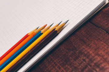 Bright used colorful pencils next to a blank sheet of paper. Work supplies stationery on a wooden texture table. Trendy minimalism. Concept of a modern freelancer workplace. Rustic cozy atmosphere