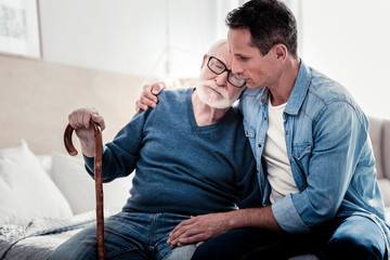 This is family. Nice pleasant aged man sitting together with his son and holding a walking stick...
