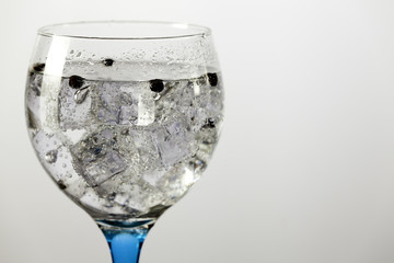 Detail gin tonic on blue glass with peppercorns
