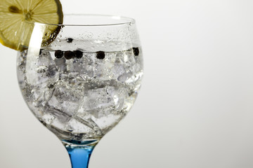 Detail gin tonic on blue glass with lemon and peppercorns
