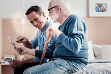 Fototapeta premium Memories from the past. Happy nice young man looking at the photograph and smiling while spending time with his father