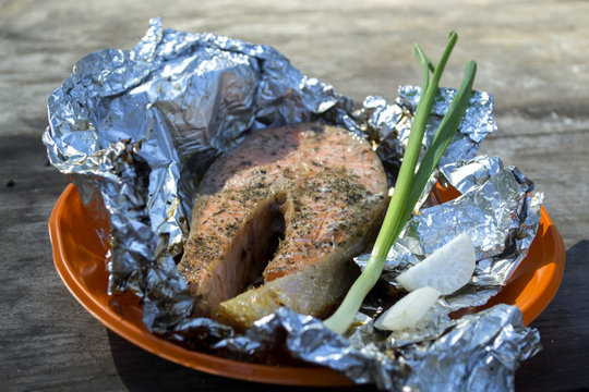 A Trout Cooked At The Stake In Orange Plate On A Wooden Table Outdoor.