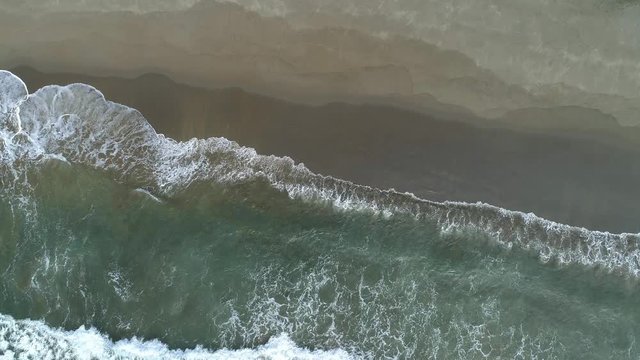 Aerial top down shot of ocean waves on sandy baech.
