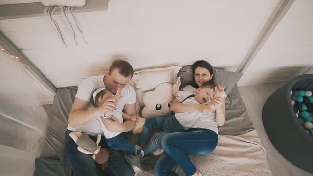 Young family have fun indoor. Happy family in white t-shirts and jeans enjoying on the bed. Top view. Family concept in white t-shirts and jeans