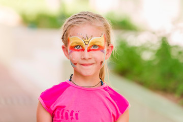 Happy little girl with face art paint in the park.