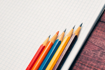 Fototapeta premium Bright used colorful pencils next to a blank sheet of paper. Work supplies stationery on a wooden texture table. Vintage minimal look. Symmetry composition. Concept of a modern freelancer workplace