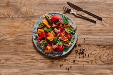 Salad with mussels, vegetables and jamon, fork with knife and peppercorns on wooden table