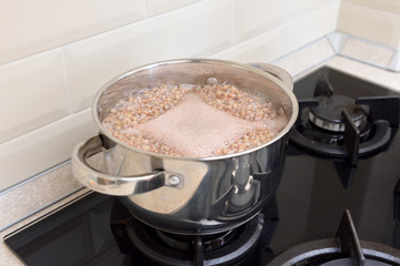 Buckwheat groats are cooked in a saucepan on a gas stove. Foam in a saucepan where buckwheat is cooked