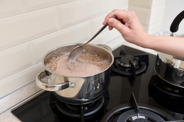 The girl's hand stirs the buckwheat in a saucepan with a spoon. Boil buckwheat