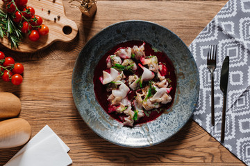 top view of delicious ceviche with dorado in plate, fork with knife and fresh tomatoes on wooden table