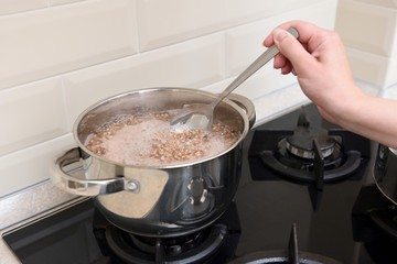 The girl's hand stirs the buckwheat in a saucepan with a spoon. Boil buckwheat