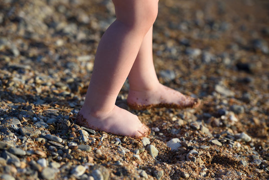 The legs of a small child. The legs of the child go along a sandy beach with pebbles to the sea