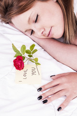 Beautiful woman sleeping near the rose flower and message on paper saying i love you