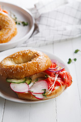 Bagels with salmon fish, cream cheese, cucumber and fresh radish slices on white wooden background