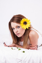 Beautiful young woman with sunflower lying in bed