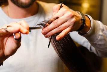 Fototapeta premium Closeup of hairdresser hands on woman's healthy hair at barber salon