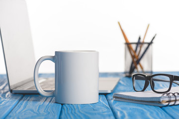 closeup shot of cup, eyeglasses on textbook, laptop and organizer with pens and pencils