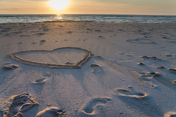 Beautiful sunset at the beach with wooden piles and hearts drawings in the sand Petten, Holland, North Sea