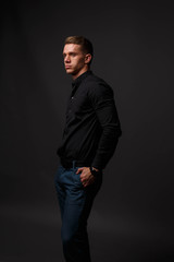 Fototapeta premium attractive white man in black shirt and blue pants stands on a dark background