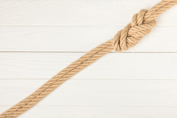 top view of brown nautical rope with knot on white wooden surface