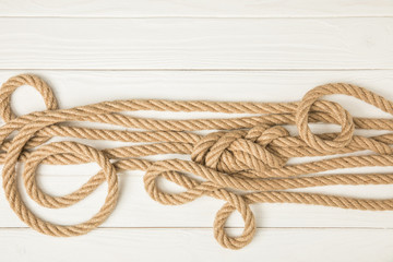 Obraz premium top view of brown nautical knotted ropes on white wooden surface