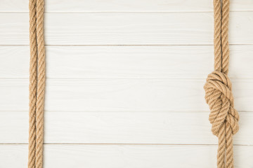 top view of frame made by brown nautical ropes with knot on white wooden background