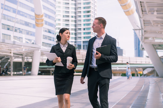 Asian business woman holding document file and plastic mug on hand talk about business future with  Caucasian businessman. they are walk together in the city.