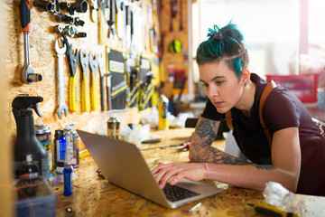 Woman using a laptop in a bicycle repair shop
 - obrazy, fototapety, plakaty
