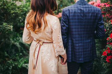 Bride and groom walk in the park in summer holding their hands