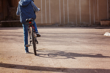 Child on a bicycle at asphalt road in sunny spring day. Back view