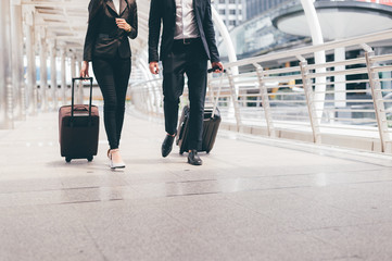 business man and businesswoman wear black suit walk together with luggage on the public street,...