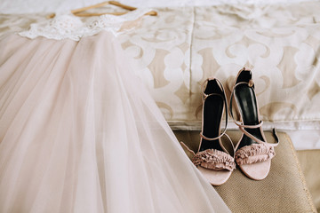 Pink elegant bride shoes next to a beautiful wedding dress lies on the bed in a hotel room. Wedding preparation