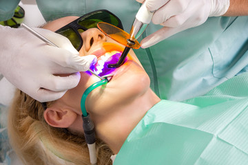 Young beautiful woman with beautiful white teeth sitting on a dental chair. The dentist cures her...