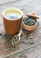 Spoon of dried green tea and a cup of brewed tea leaves on wooden background