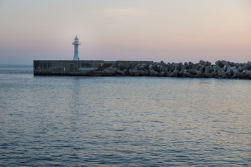 Fototapeta premium Seawall with wavebreakers with white lighthouse during dawn in Seogwipo, Jeju Island, South Korea