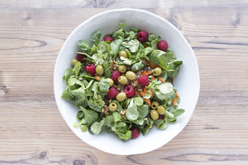 Salad of canons, raspberries, raisins, olives, nuts, carrots and pips on wooden background