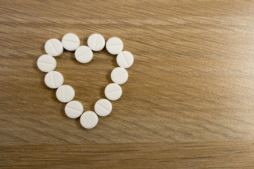 Fototapeta na wymiar Heart-shaped pills on a light wooden table close-up
