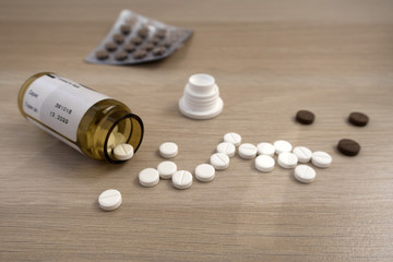 Tablets scattered from a jar on a light wooden table close up