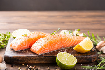 Fresh raw salmon fillet with aromatic herbs, spices on old wooden background with copy space.