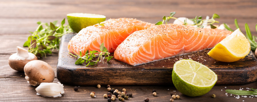 Fresh raw salmon fillet with aromatic herbs, spices on old wooden background with copy space. Banner.