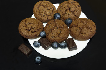 Chocolate cookies with chocolate pieces and blueberries on a white saucer, isolated on dark background.