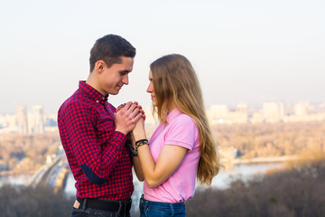 Fototapeta premium The guy holds the girl's hands in his against the backdrop of the cityscape