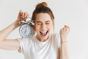 Cheerful woman in casual clothes holding alarm clock and rejoices - obrazy, fototapety, plakaty