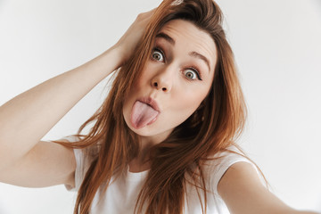 Fototapeta premium Funny woman in casual clothes making selfie while showing tongue