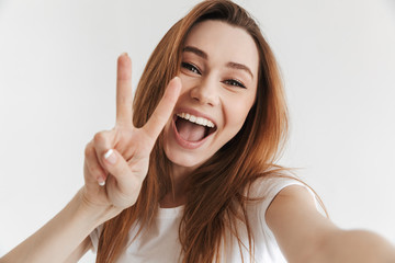 Woman in casual clothes making selfie while showing peace gesture