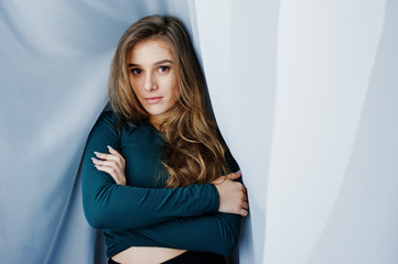 Handsome brunette girl wear on green, posing at curtains. Studio model portrait.