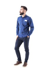 Fototapeta premium Cool relaxed young bearded business man with hands in pocket and mobile phone in shirt pocket looking away. Full body isolated on white background. 
